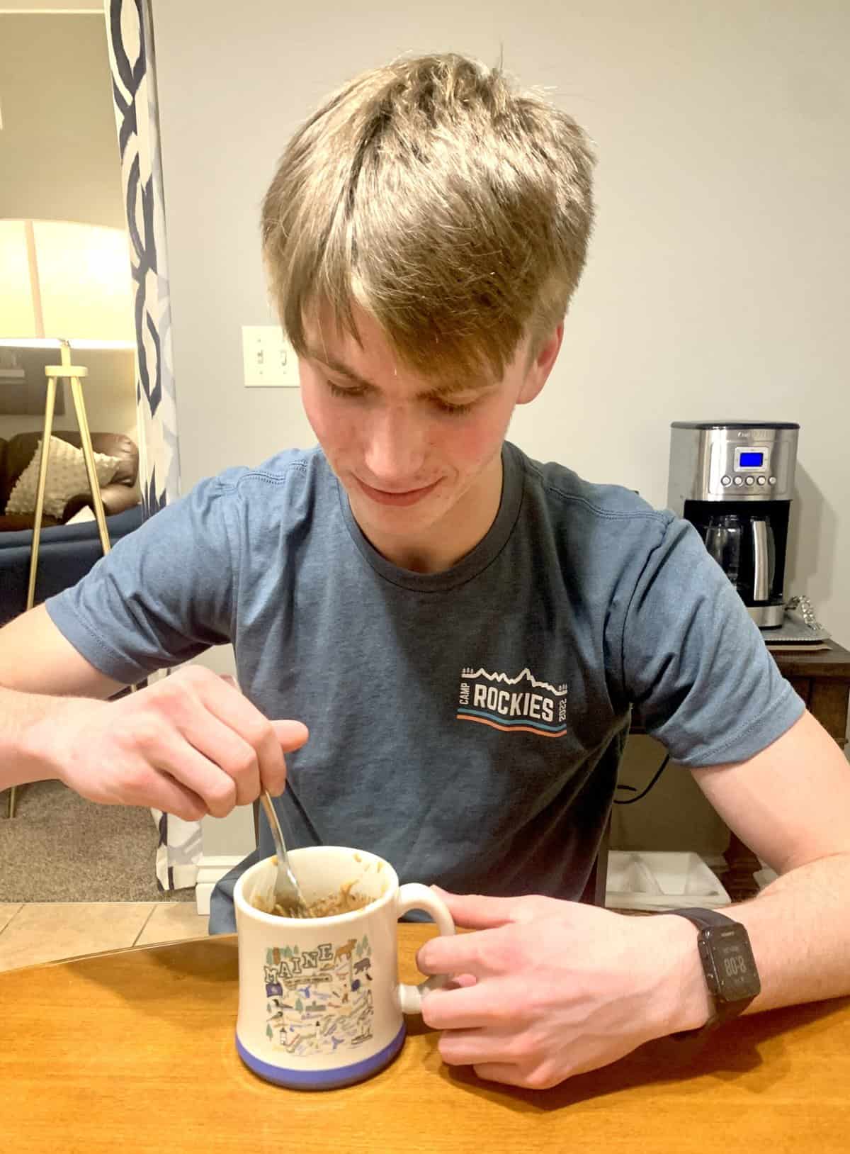 A teen boy eating mug cake at a table.