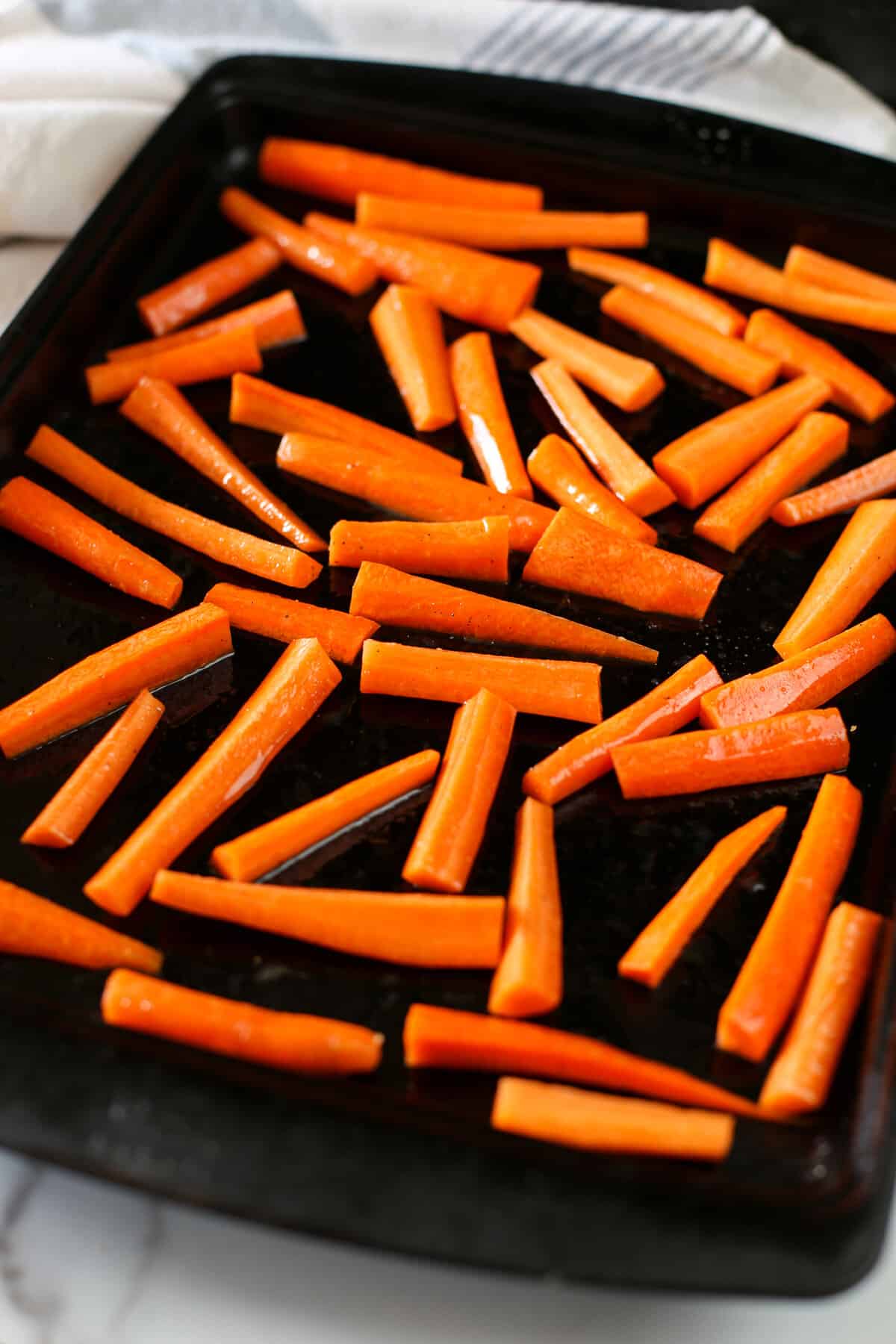 Raw carrot slices tossed in butter and maple syrup laid out on a roasting pan.