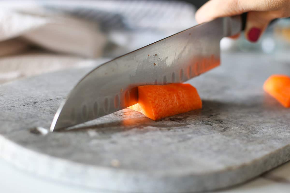 A knife slicing into a carrot on a cutting board.