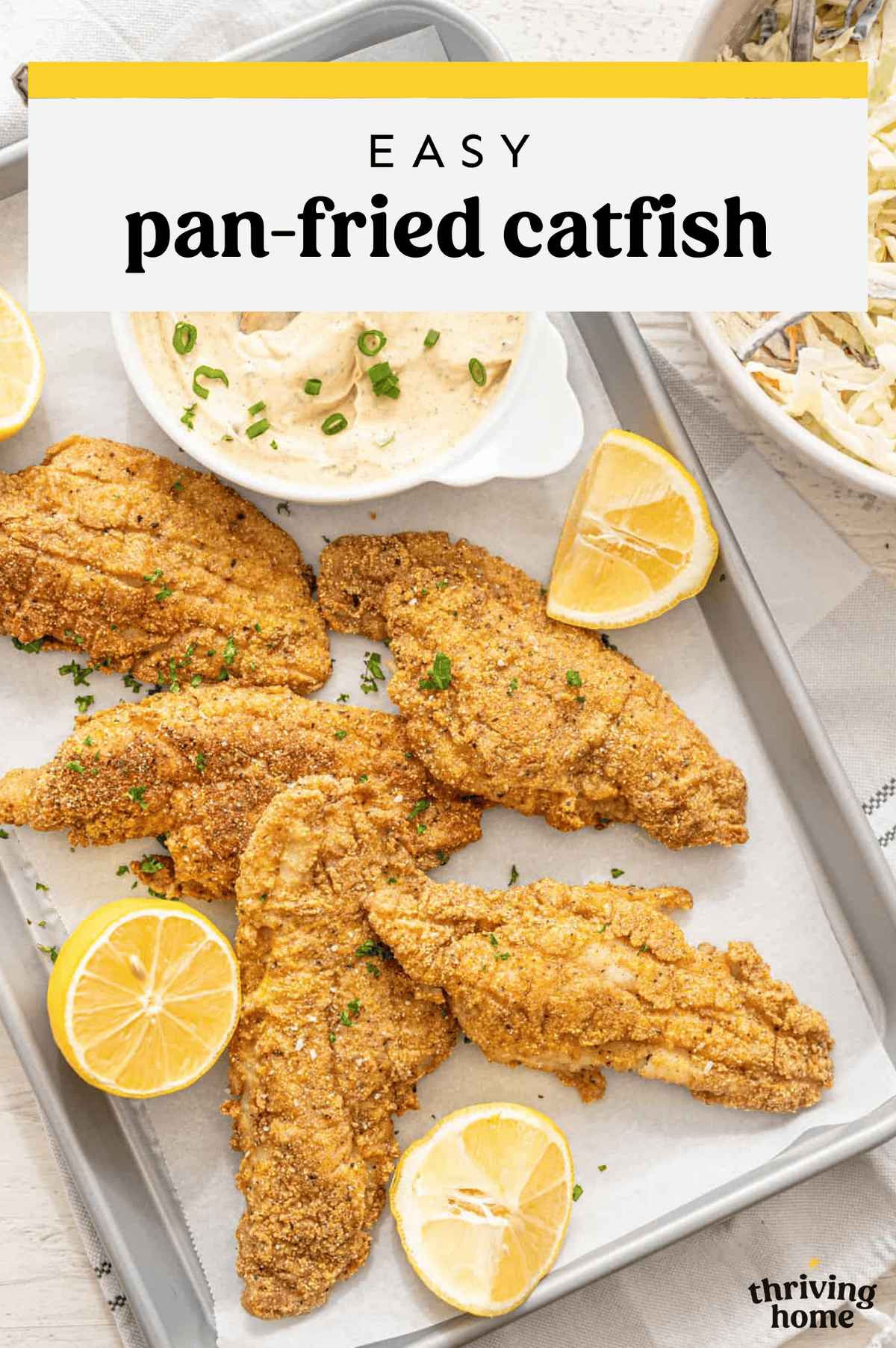 Pan fried catfish filets on a parchment-lined baking sheet with lemon wedges.