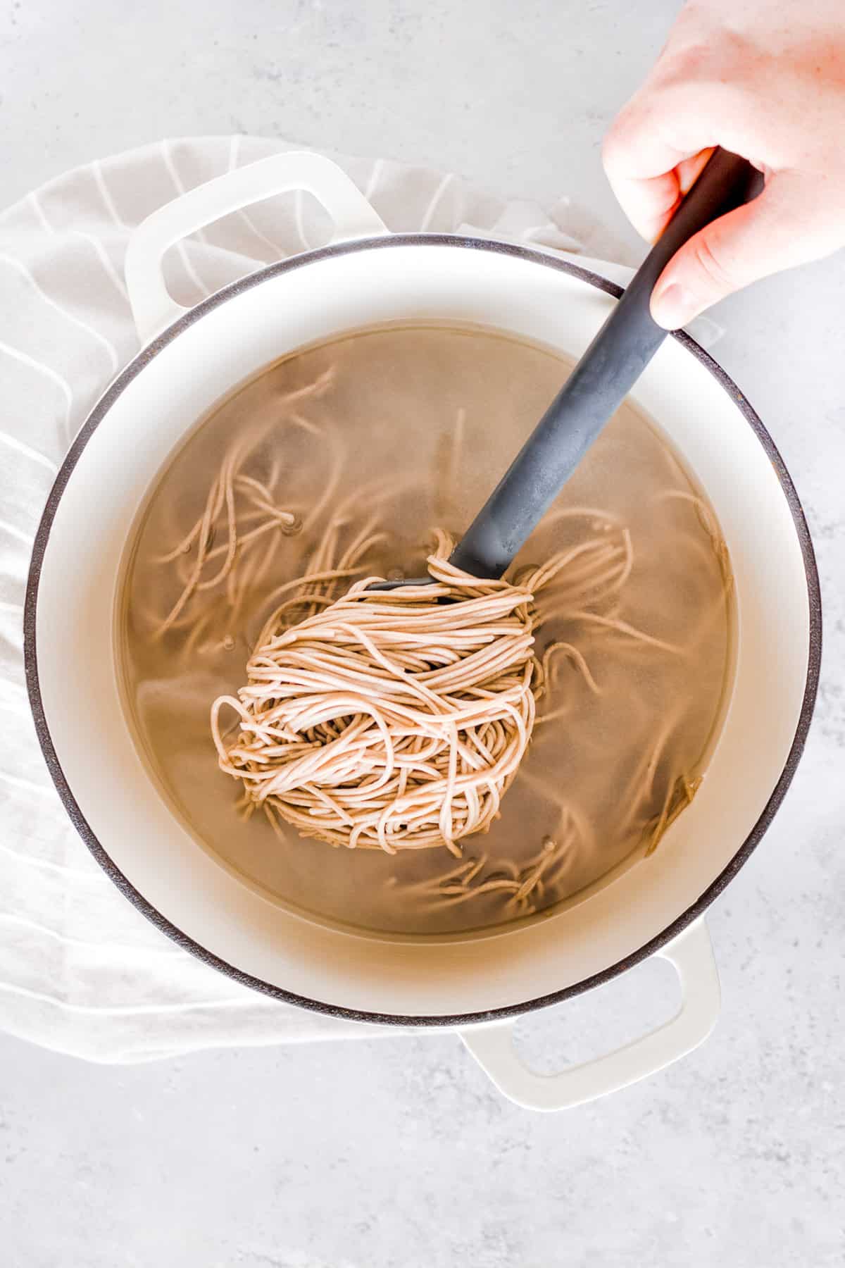 Soba noodles being cooked in a white pot.