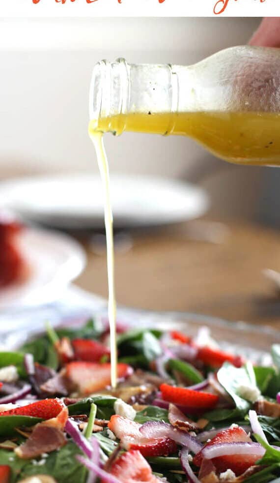 Lemon Honey Vinaigrette being drizzled over a spinach salad on a table.