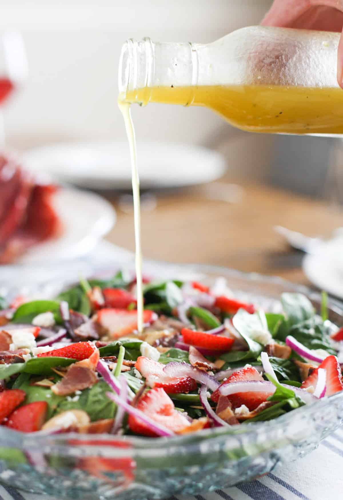 Lemon honey vinaigrette being poured onto a spinach salad with bacon, cheese, red onion, and strawberries on top.