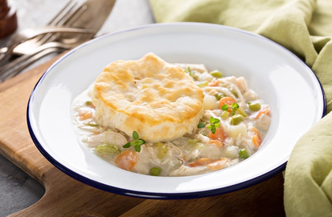 Chicken pot pie filling in a bowl with a biscuit on top.