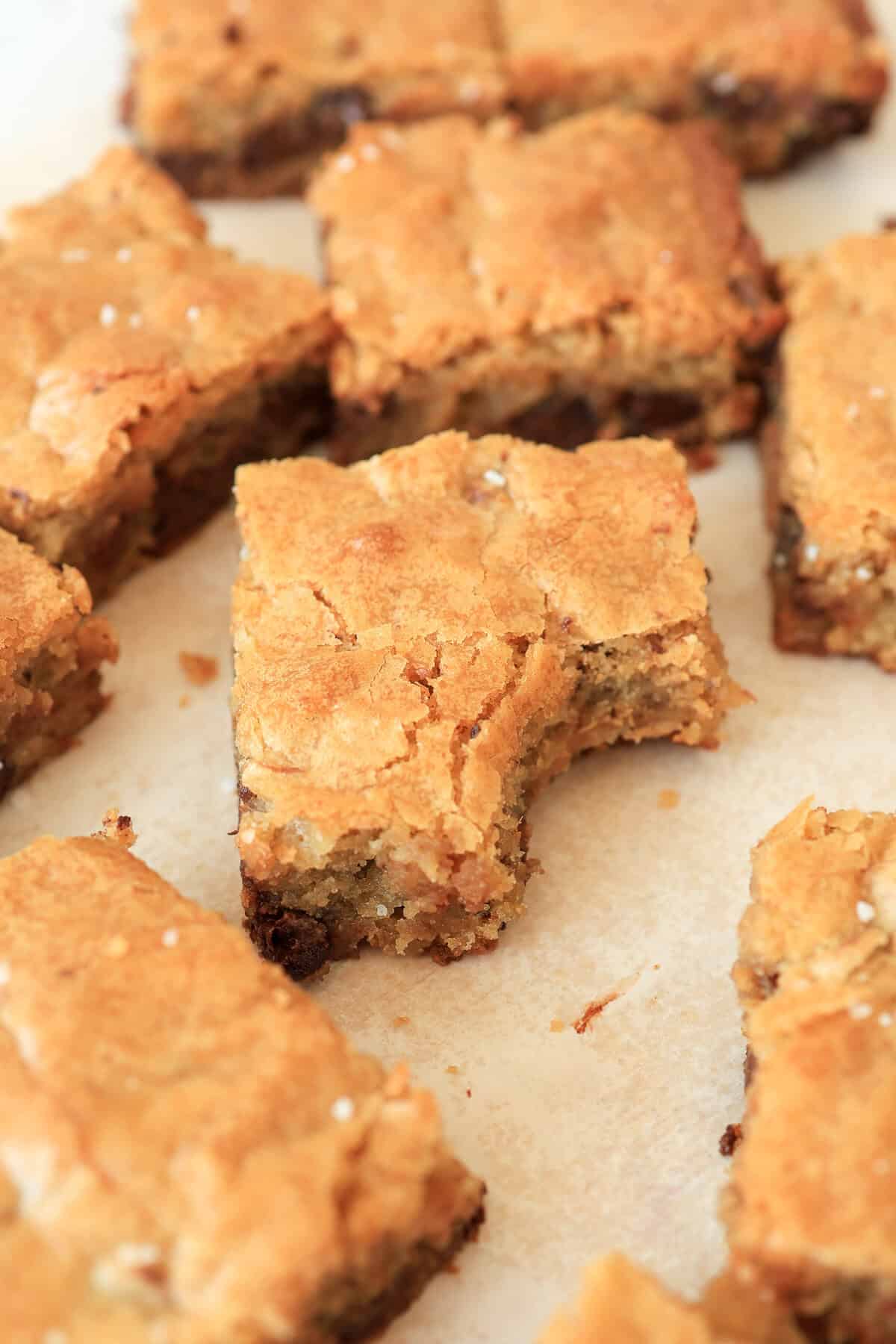 A couple of blondie brownies on a platter with one having a bite taken out of it.
