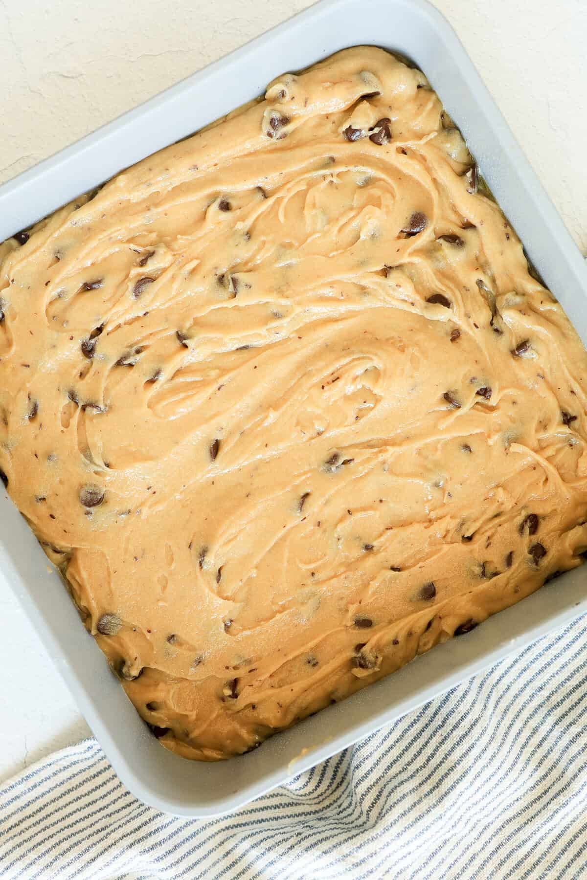 A square baking dish with cookie dough spread in it.