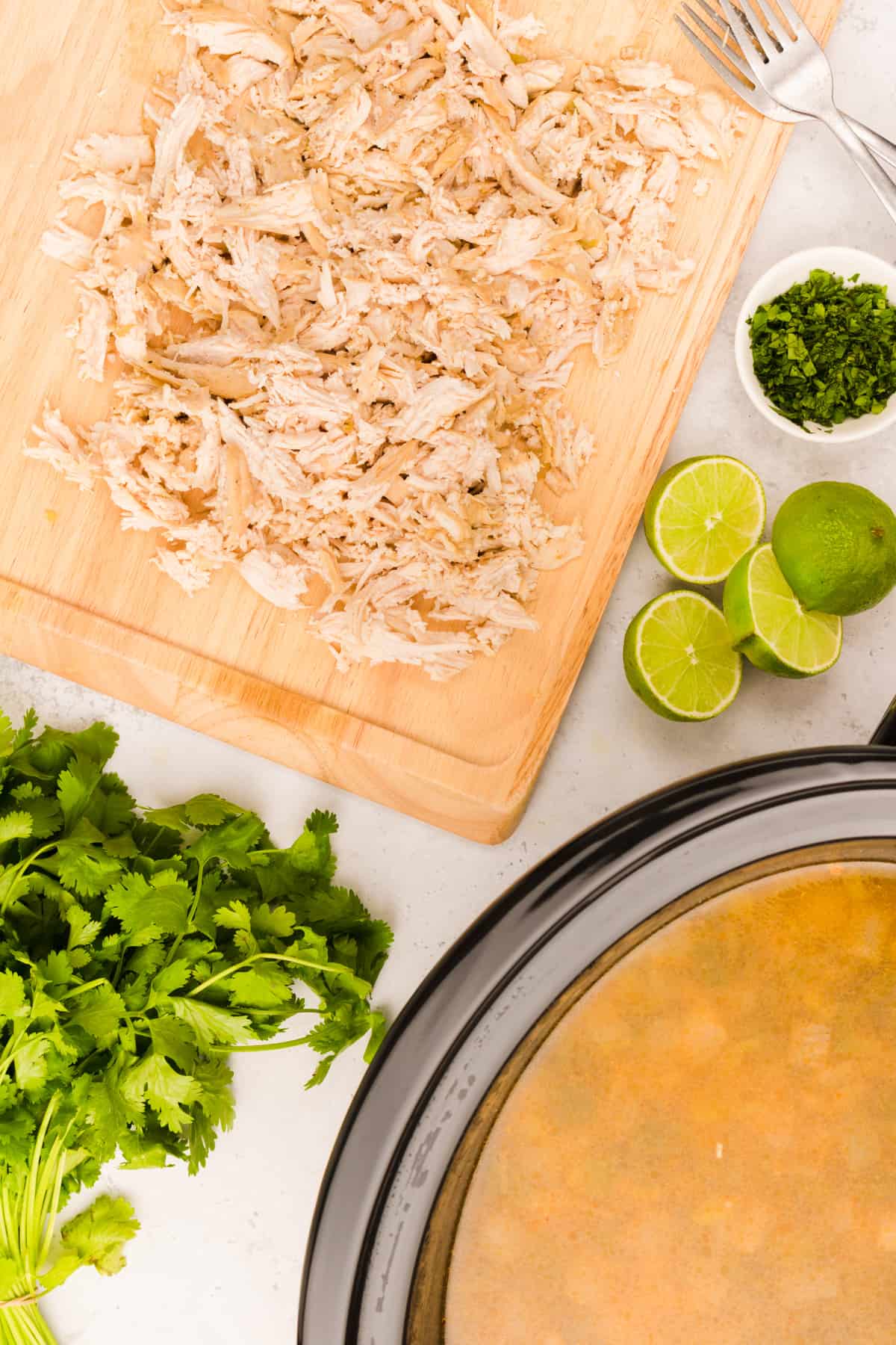 shredded chicken on a wooden cutting board next to a crockpot