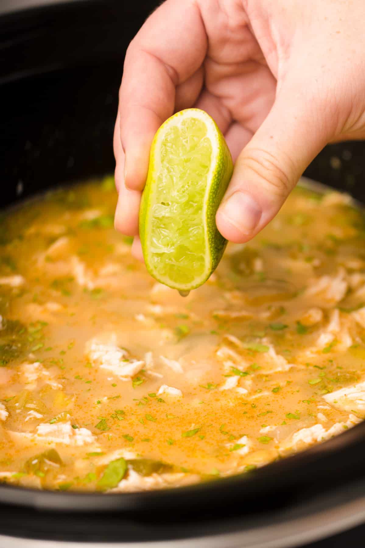 Hand squeezing a lime into chicken chili in a crockpot.