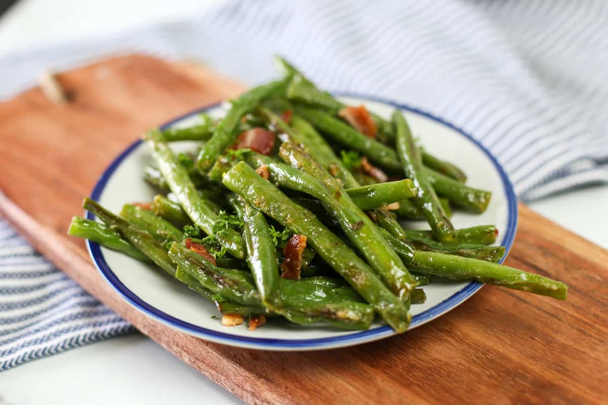 Garlic green beans on a small plate with crumbled bacon on top.