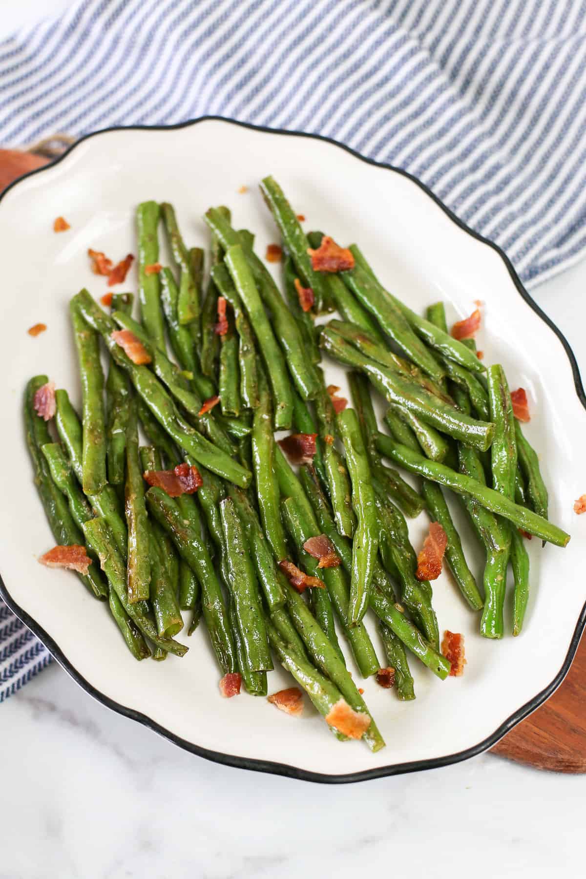 Garlic green beans on a white serving platter with bacon sprinkled on top.