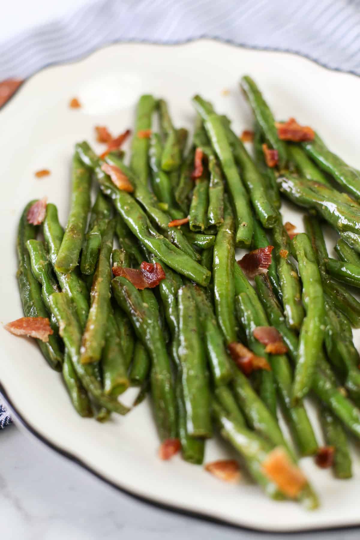 Garlic Green Beans served on a white plate with bacon pieces sprinkled on top.
