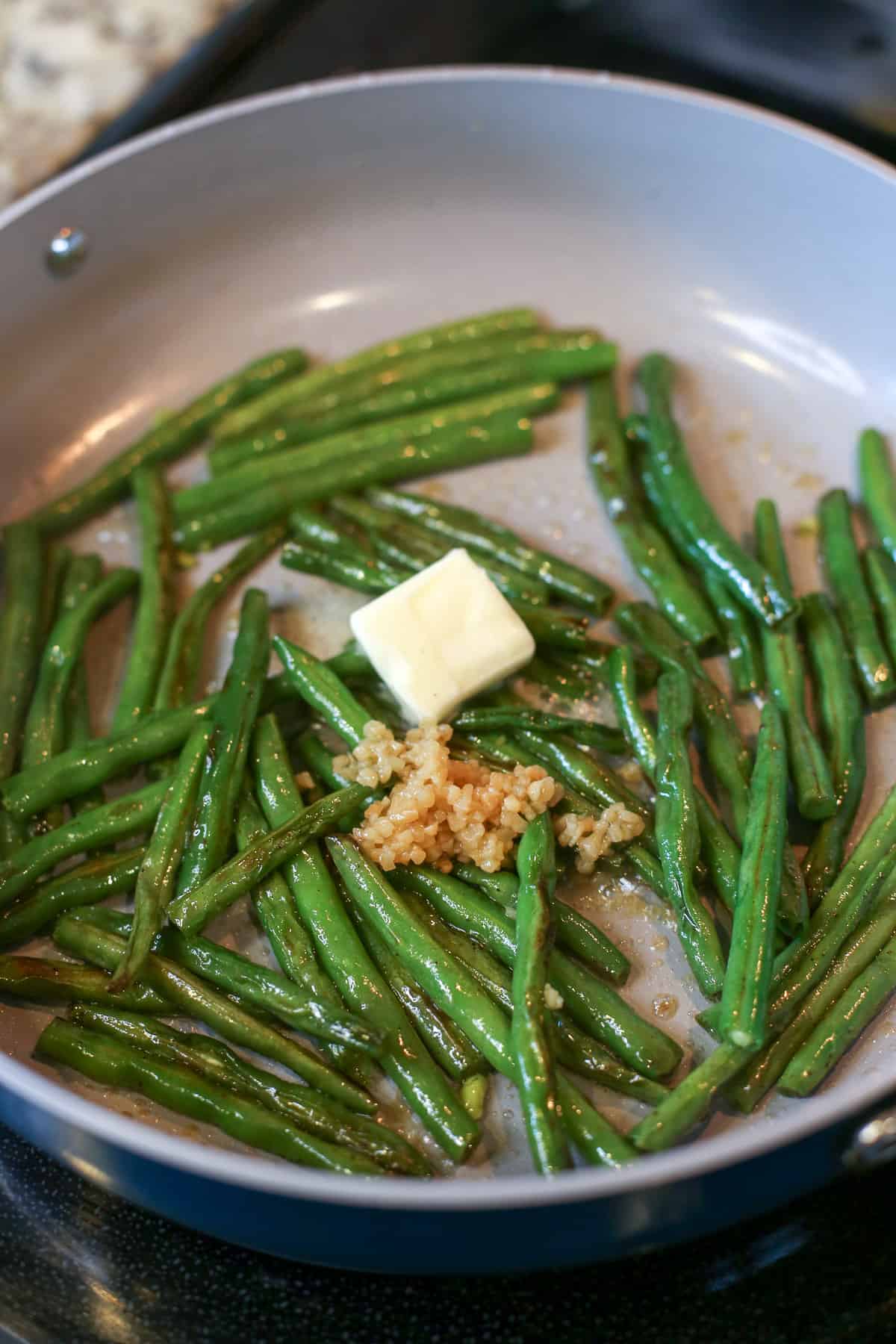 Butter and garlic added to sauteed green beans in ceramic pan.