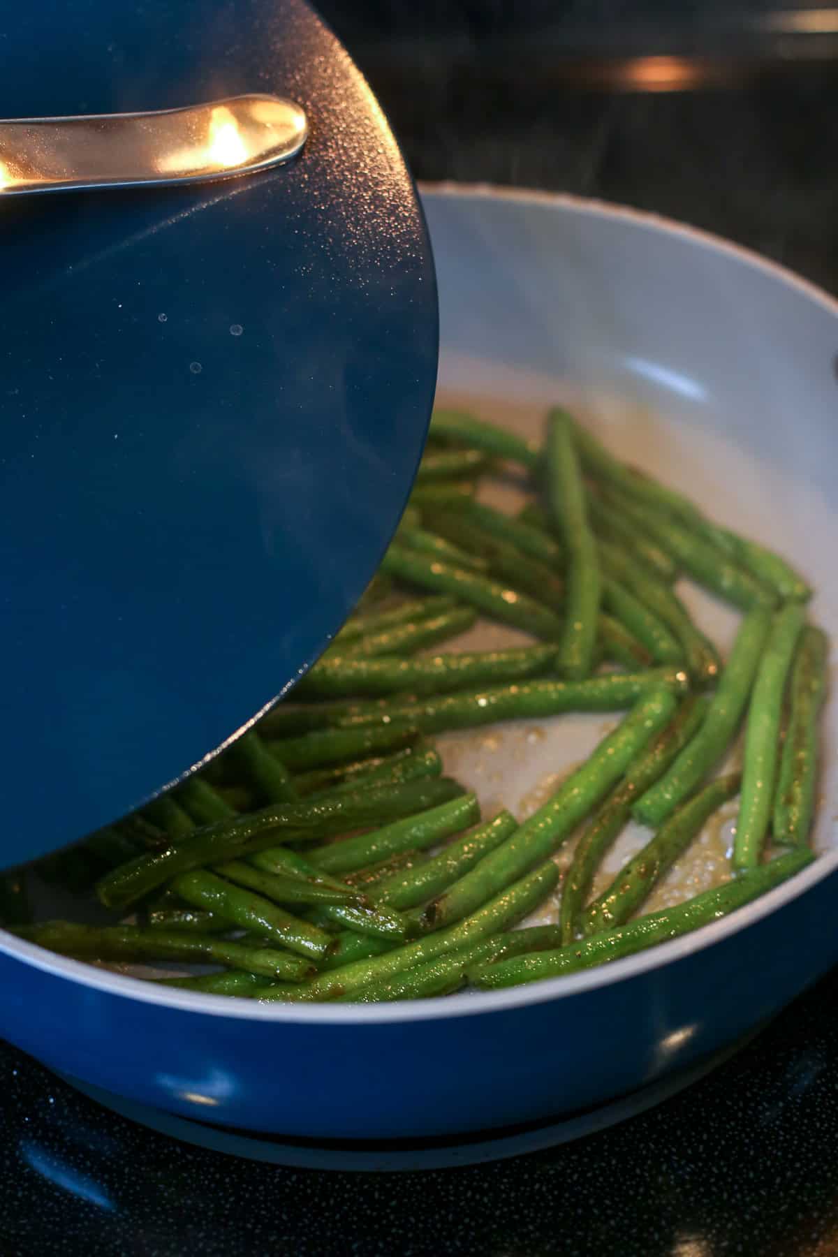 Sauteed green beans in a blue ceramic saute pan with a lid about to be put on top. 