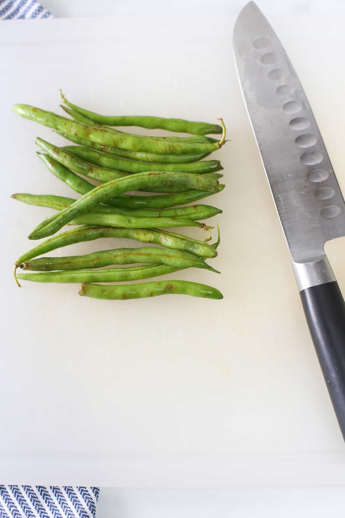 Fresh green beans lined up on a cutting board with a knife next to them.