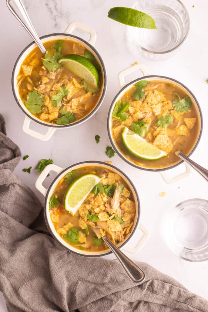 white bean chicken chili in three bowls with cilantro and lime wedges on top