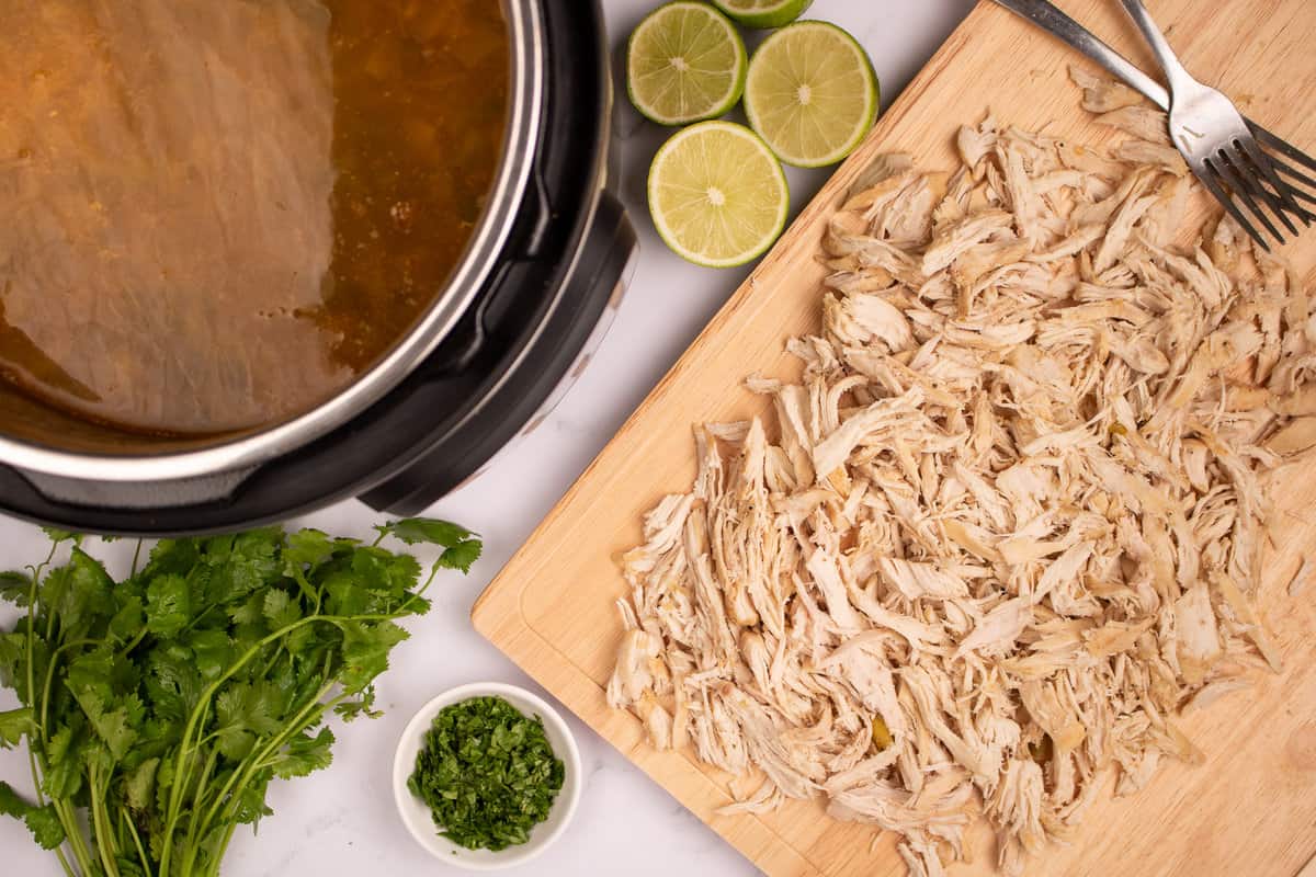 shredded chicken on a wooden cutting board next to Instant Pot