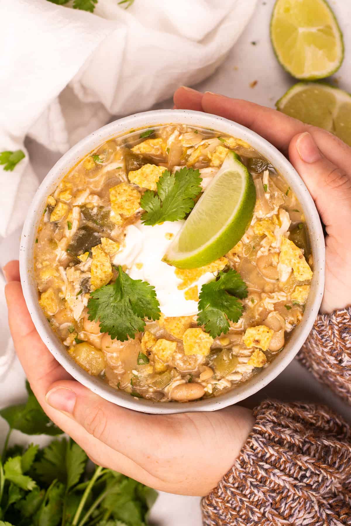 Hands holding healthy white chicken chili in a bowl.