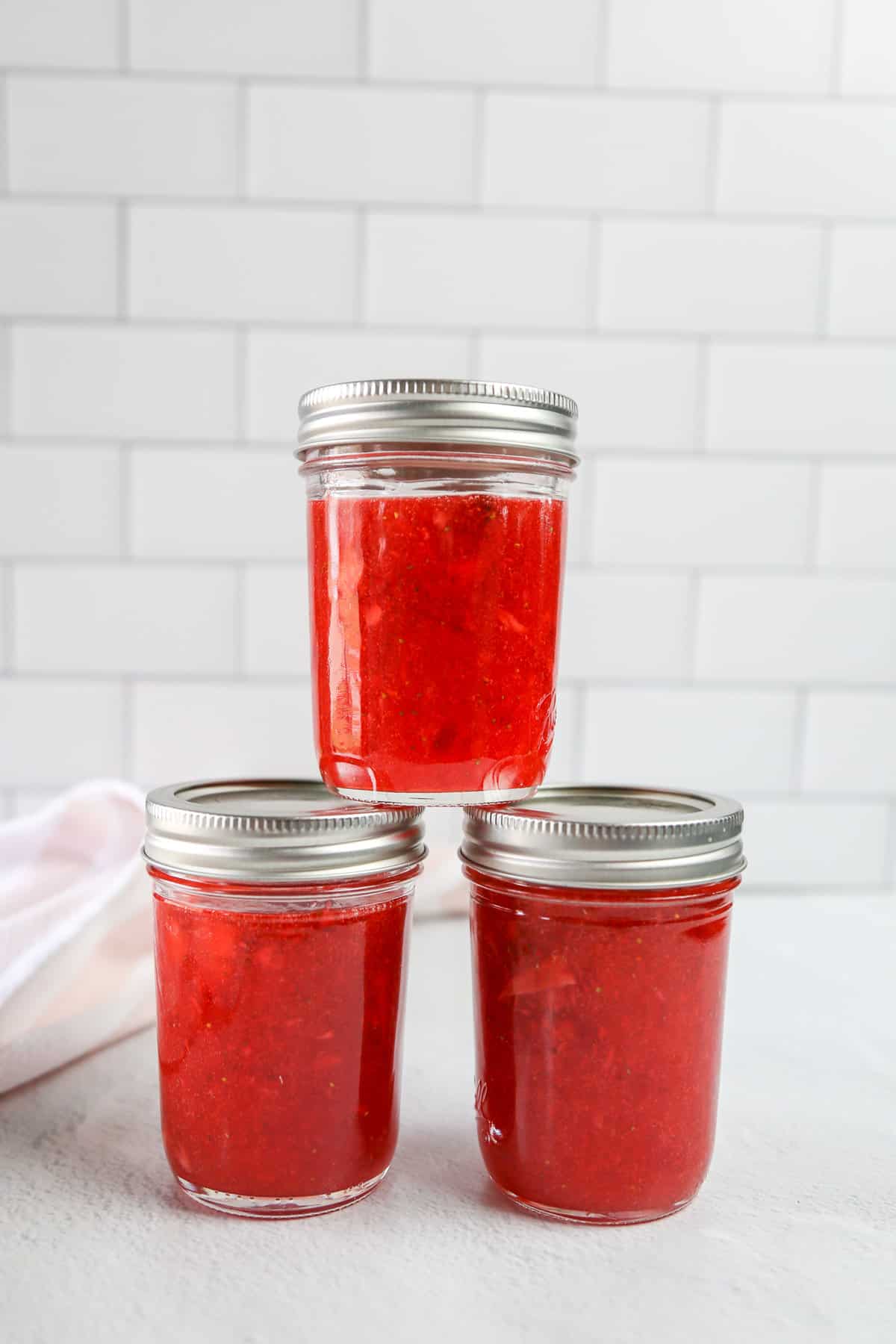 A stack of 8-ounce mason jars full of strawberry freezer jam cooling on the counter.