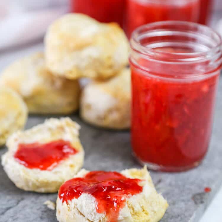 Strawberry freezer jam on a biscuit with full jars in the background.