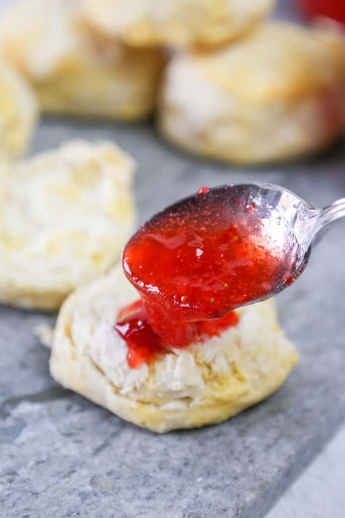 A spoon scooping strawberry freezer jam on a biscuit