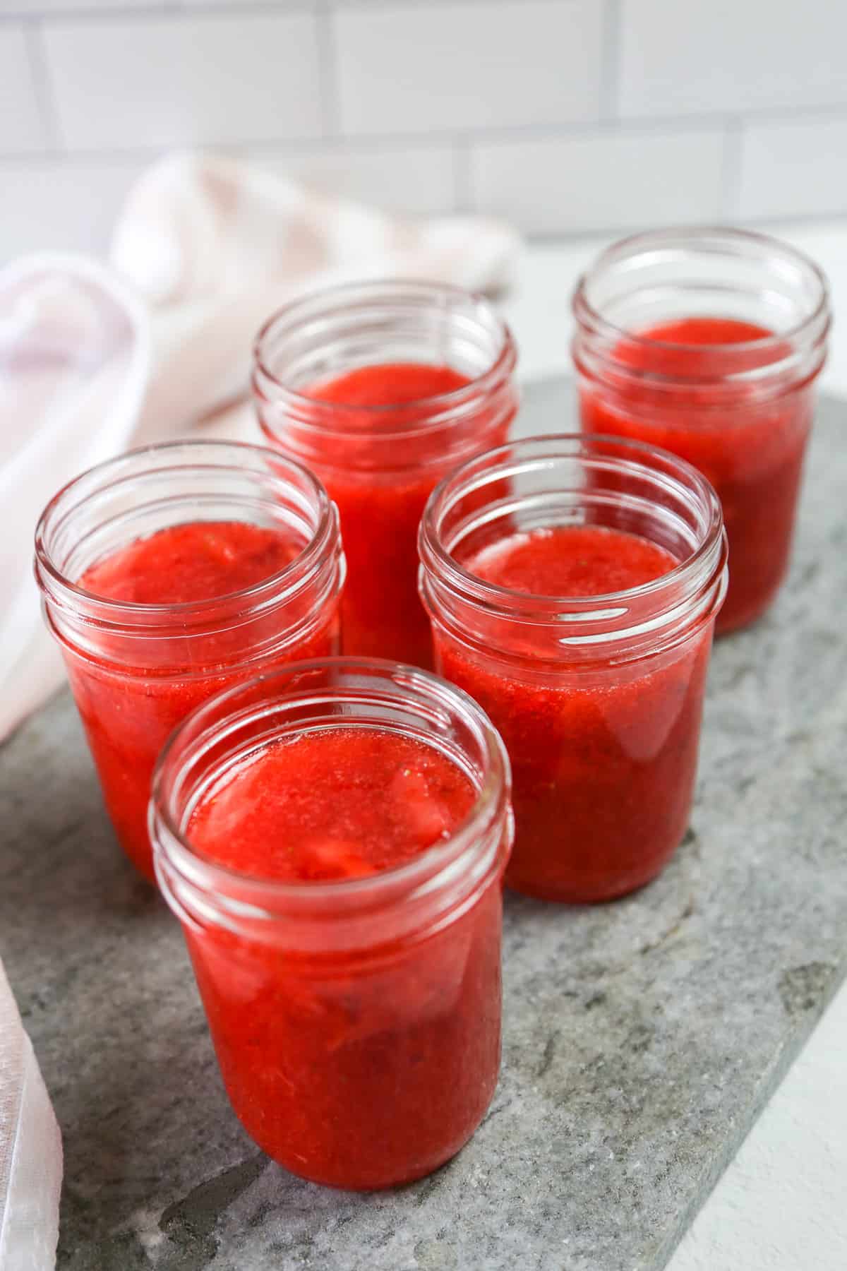 Jars of strawberry freezer jam without lids cooling on a counter.