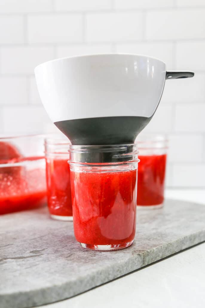 Adding strawberry jam to an 8 ounce jar using a funnel