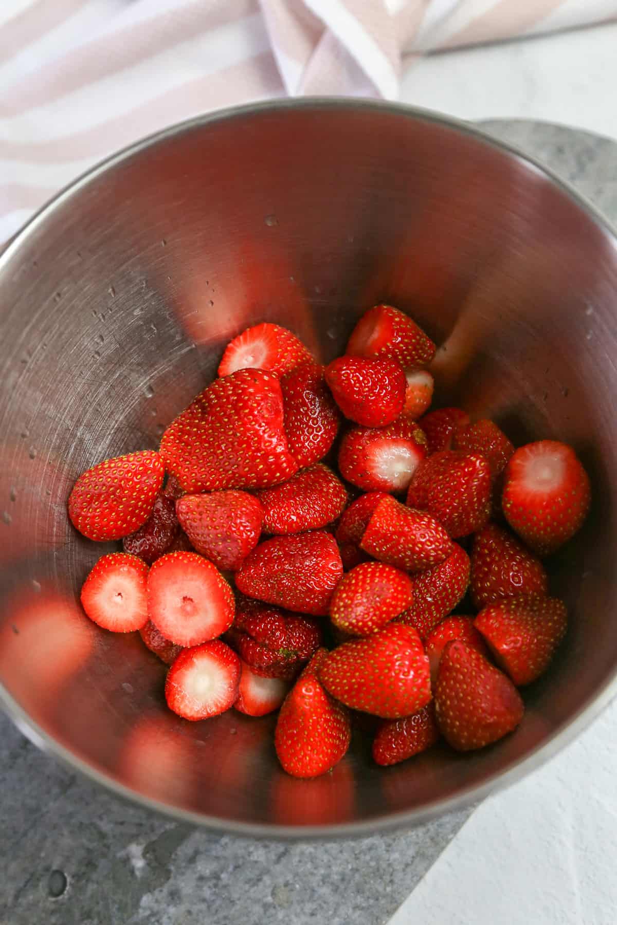 Strawberries, washed with tops removed in a metal mixing bowl.