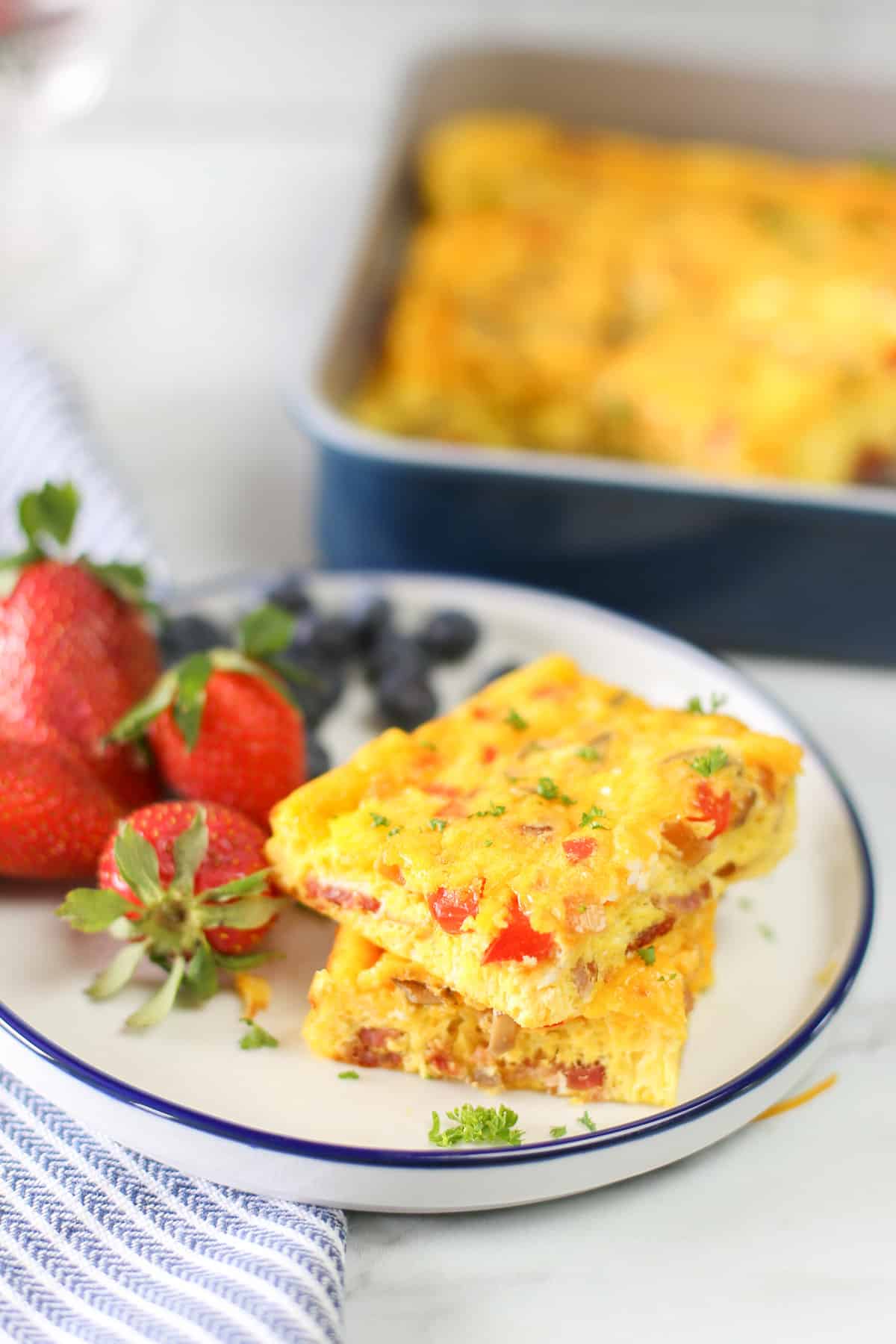 Baked omelette slices stacked on a plate with fruit.