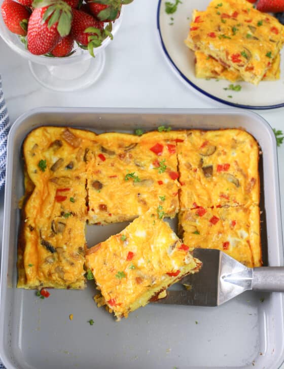 Baked omelette in a baking pan cut into servings with one square being lifted out with a spatula.