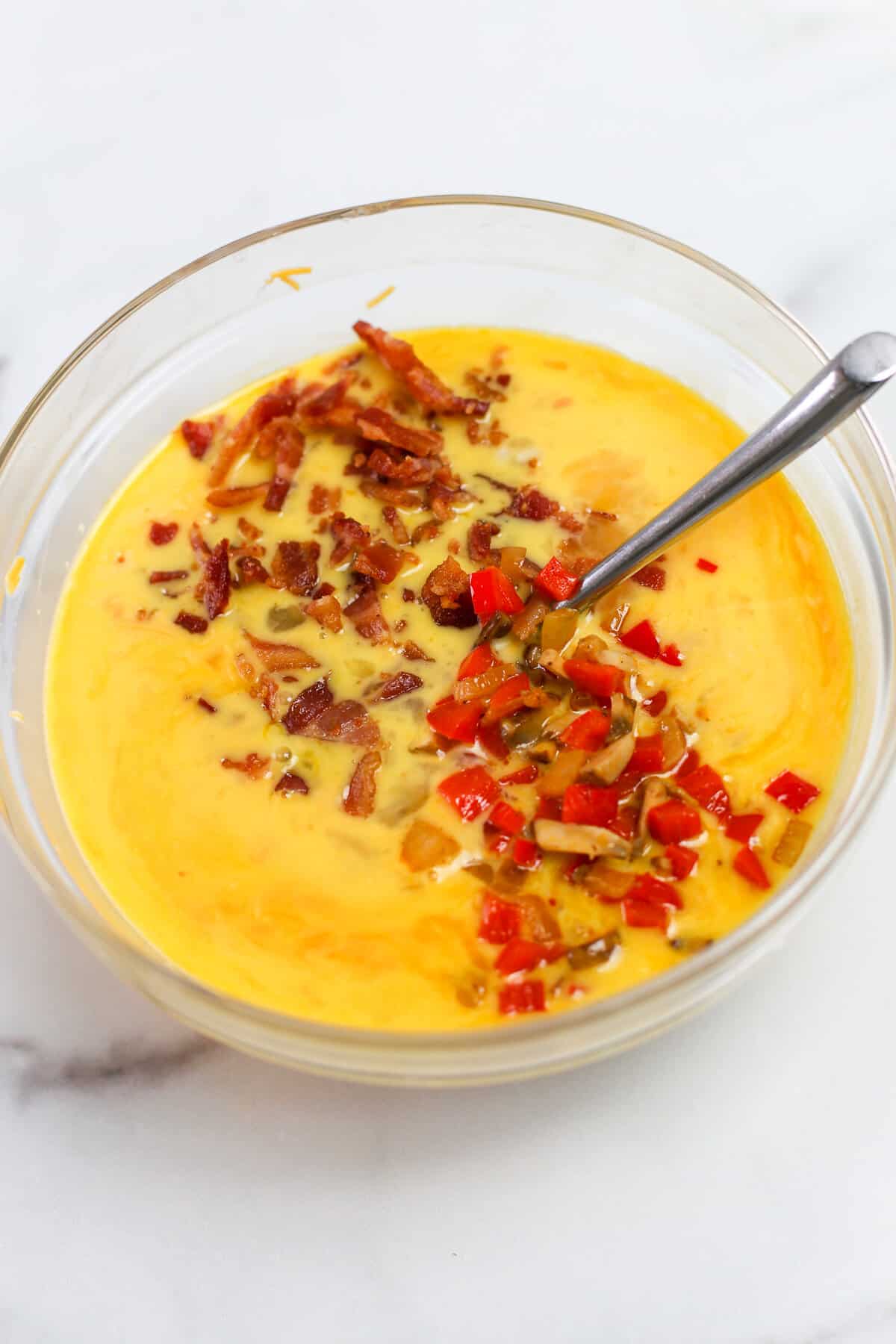 Stirring bacon and chopped red pepper to the wet ingredients for a baked omelette.