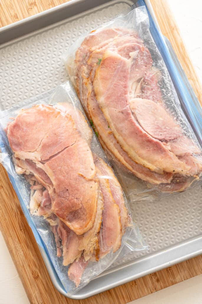 Spiral sliced ham pieces in two freezer bags lying on a baking sheet.