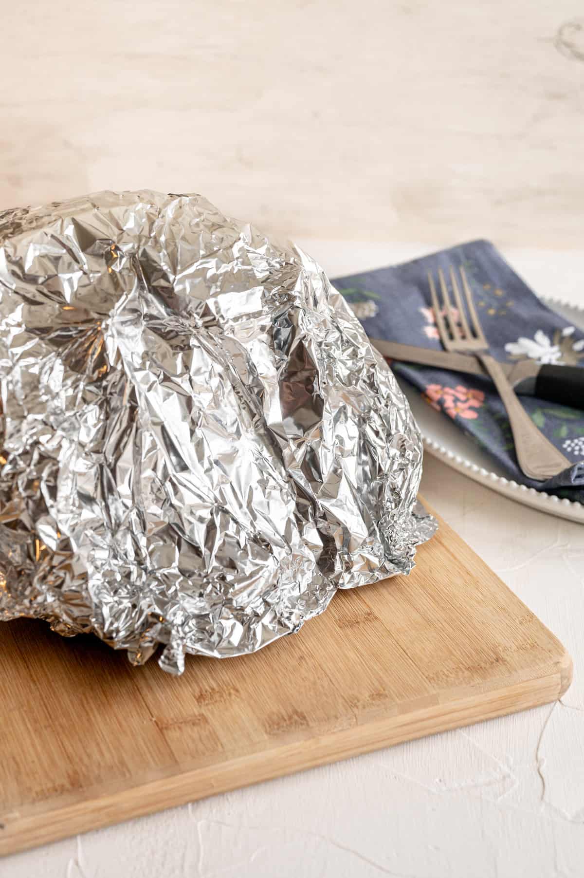 Foil covering a crock pot ham that is resting on a cutting board after cooking.