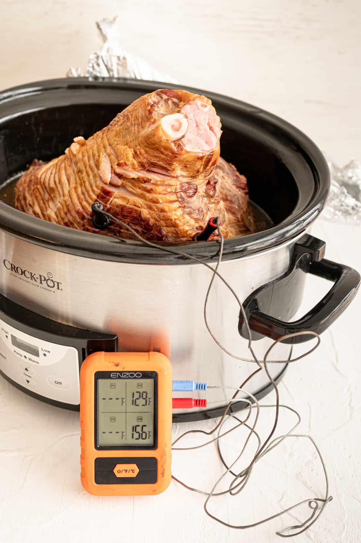 Bone-in ham in a slow cooker with a meat thermometer in it.