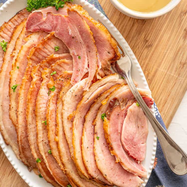 spiral sliced crockpot ham slices on a platter with pineapple sauce on the side