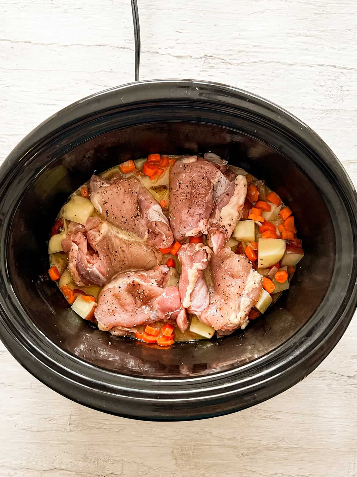 Chicken thighs and sauteed veggies in a slow cooker before cooking.