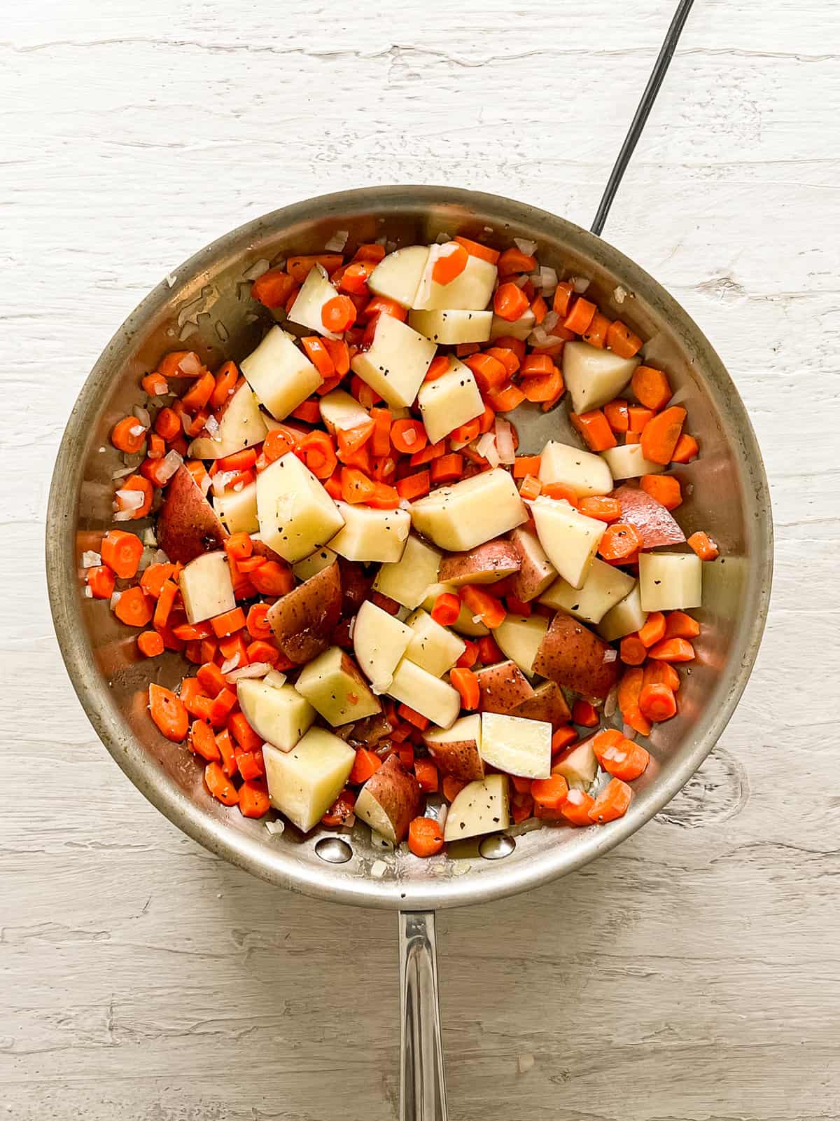 Sautéed carrots, onions, and red potatoes in a frying pan.