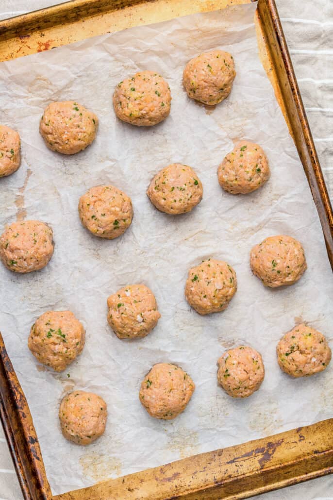 Placing baked ground turkey meatballs on a baking sheet