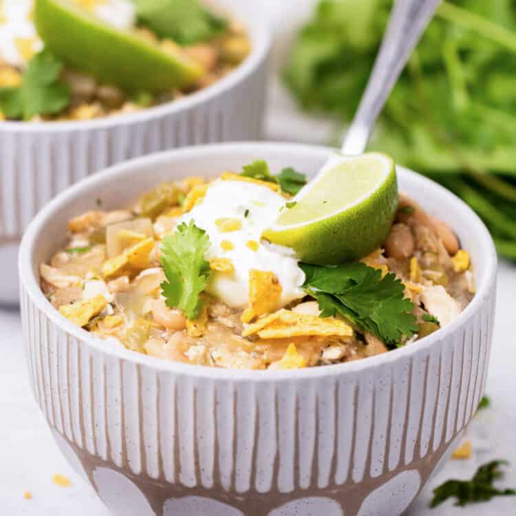 A bowl of white chicken chili with sour cream, crushed tortillas, and a lime wedge on top.