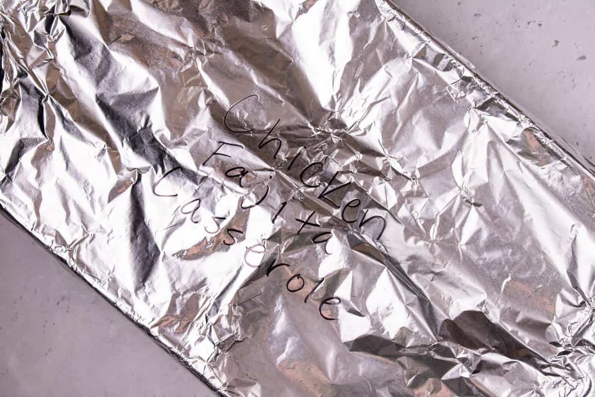 A 9x12 baking dish covered in foil and labeled chicken fajita casserole.