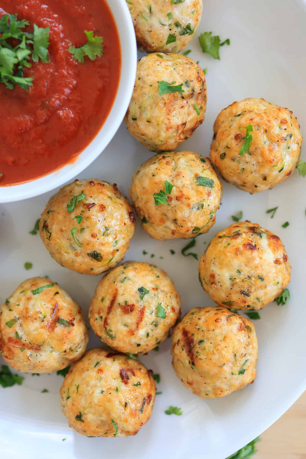 Turkey meatballs on a white plate with a bowl of marinara sauce.