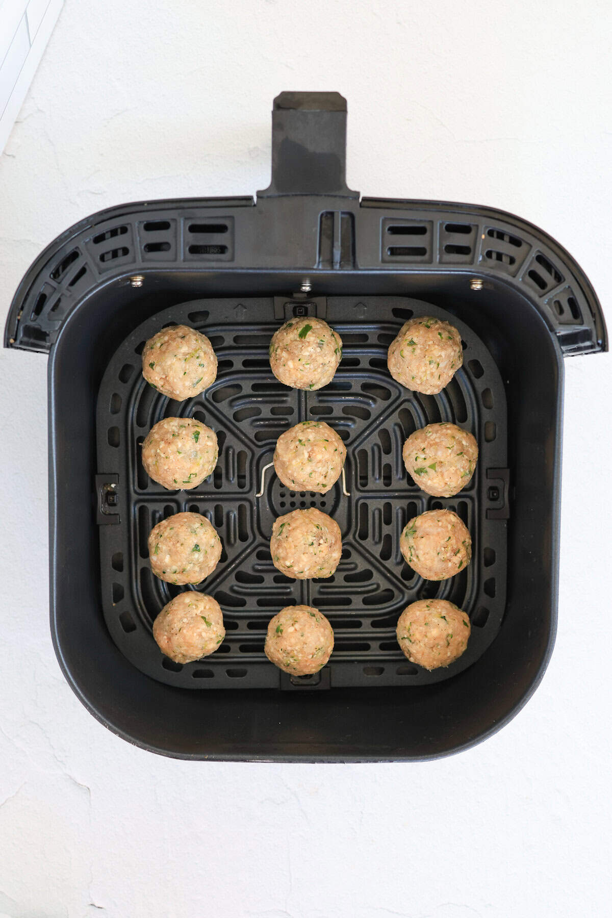 Raw turkey meatballs with sneaky zucchini in an air fryer basket.