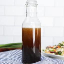 Asian Sesame Salad Dressing in a glass jar with a slaw salad in the background