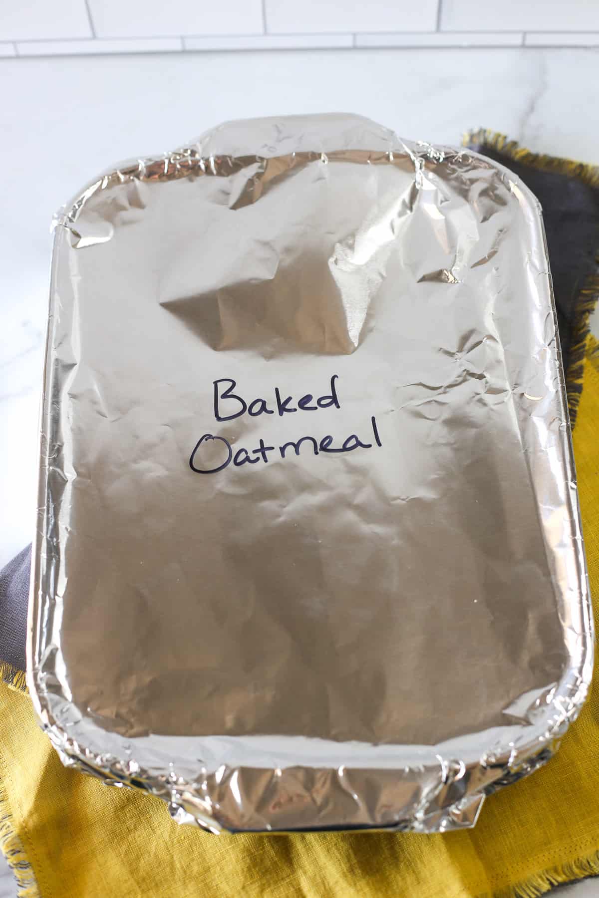 A casserole dish covered with foil and labeled Baked Oatmeal.