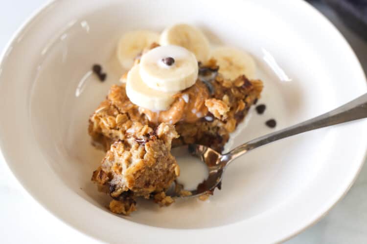 Banana baked oatmeal serving in a bowl with milk, banana slices and mini chocolate chips.