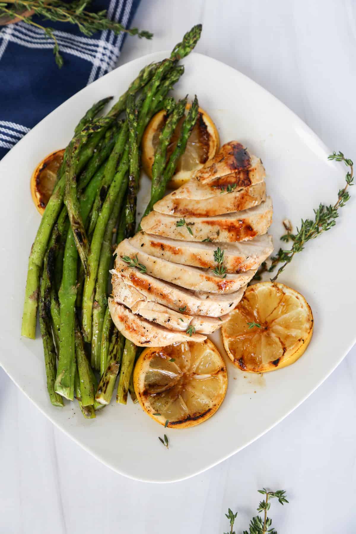 Grilled Lemon garlic chicken sliced and laying on top of grilled asparagus and lemon slices.