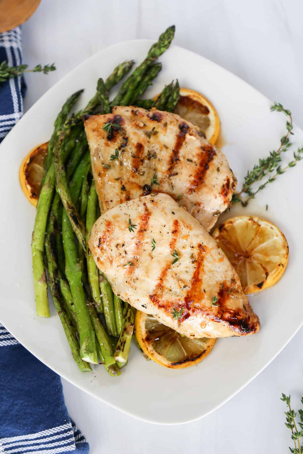 Grilled lemon garlic chicken on top of grilled asparagus and lemon slices on a white plate.