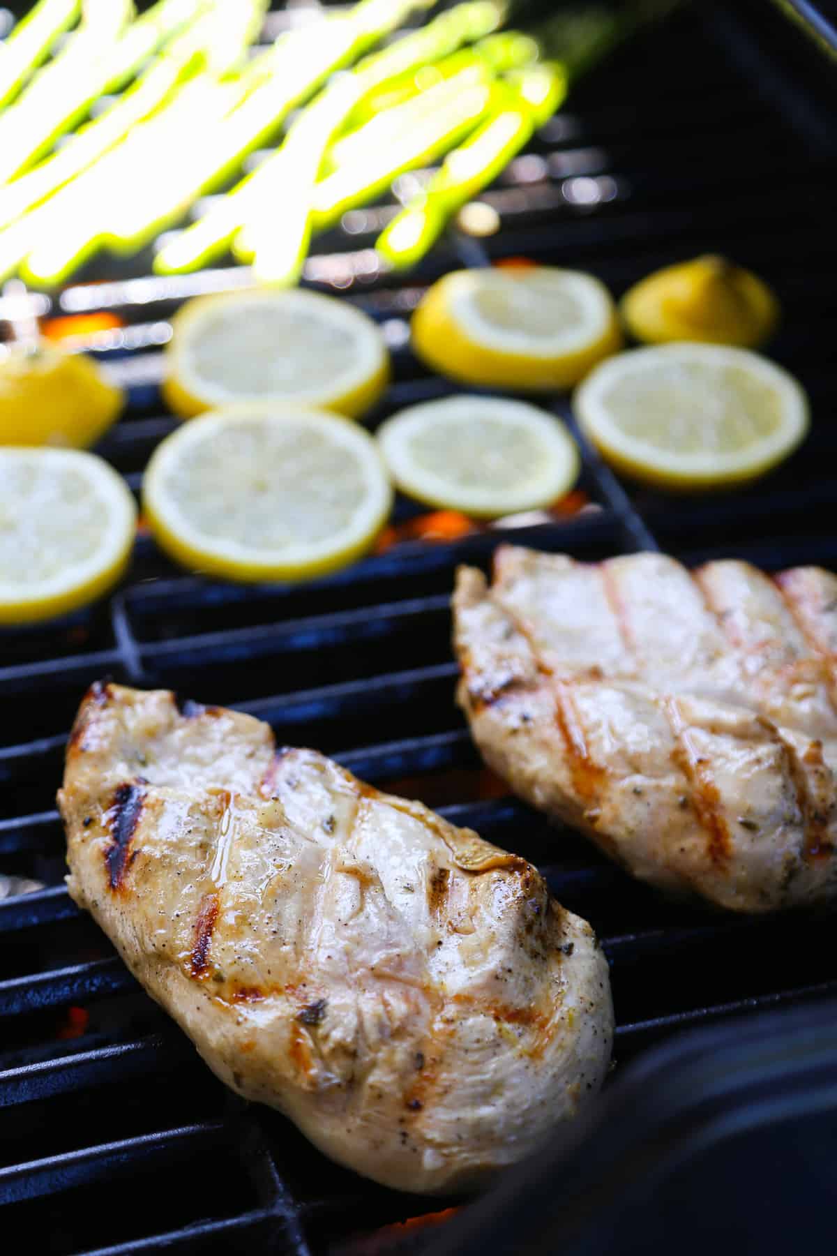 Lemon Garlic Chicken and lemon slices cooking on a grill.