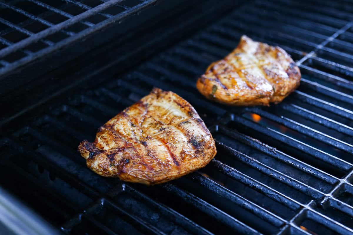 Marinated chicken grilling on the grates of a grill.