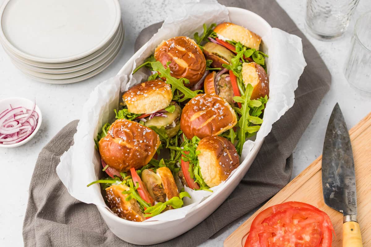 A basket full of mini chicken burgers on pretzel buns.