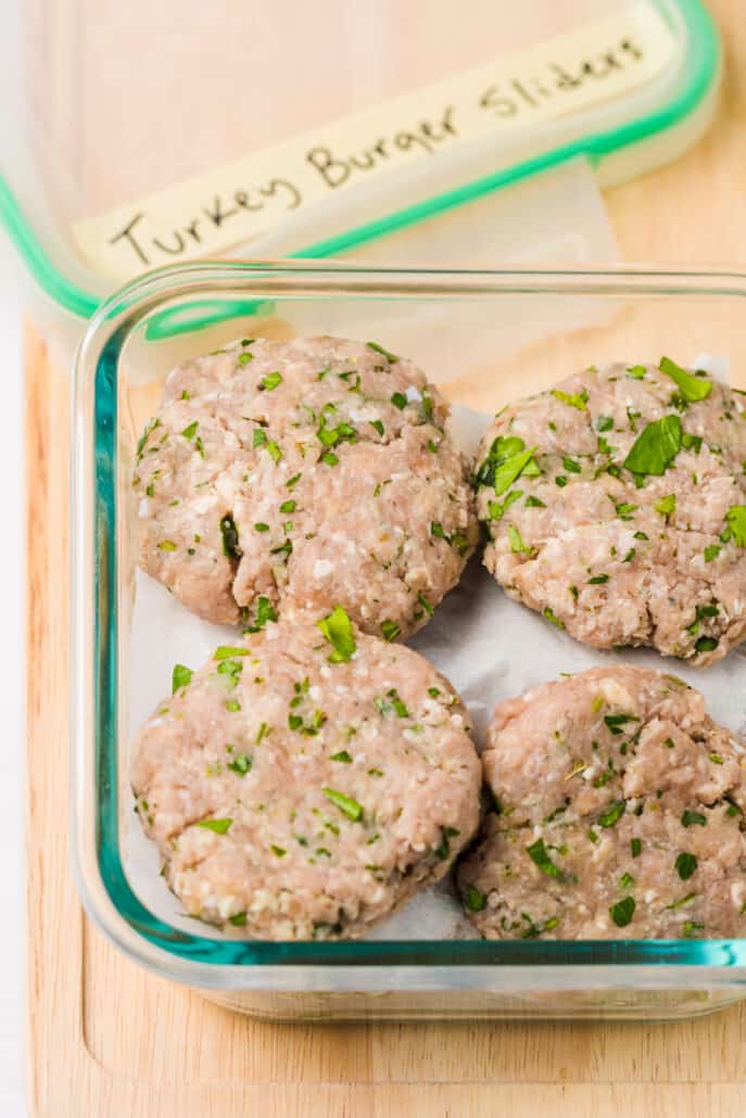 Turkey burger sliders prepped and sitting on parchment paper in a freezer-safe container.